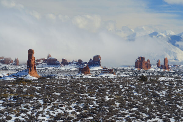 A Collection Of Arches And Pillars Towers Over The Foreground As A Background Snowstorm Engulfs The La Sal Mountains Of Utah