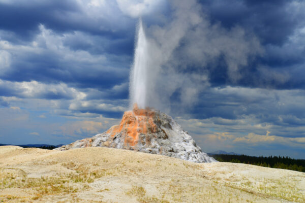 White Dome Geyser Erupts In Low Light Under A Dark Cloud Deck On A Rainy Day Over The Lower Geyser Basin Of Yellowstone National Park, Wyoming