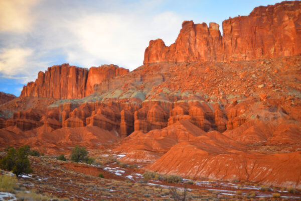 The Tall Cliff Wall Rises Up Through Several Different Terrain Types While Illuminated Red By The Sunset Over Capitol Reef National Park, Utah