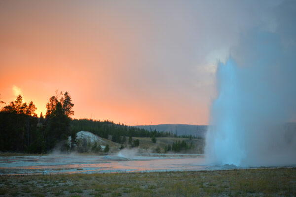 An Eruption Of Daisy Geyser Appears Blue Under Heavy Rain Lit Orange By Sunset Over The Upper Geyser Basin Of Yellowstone National Park, Wyoming